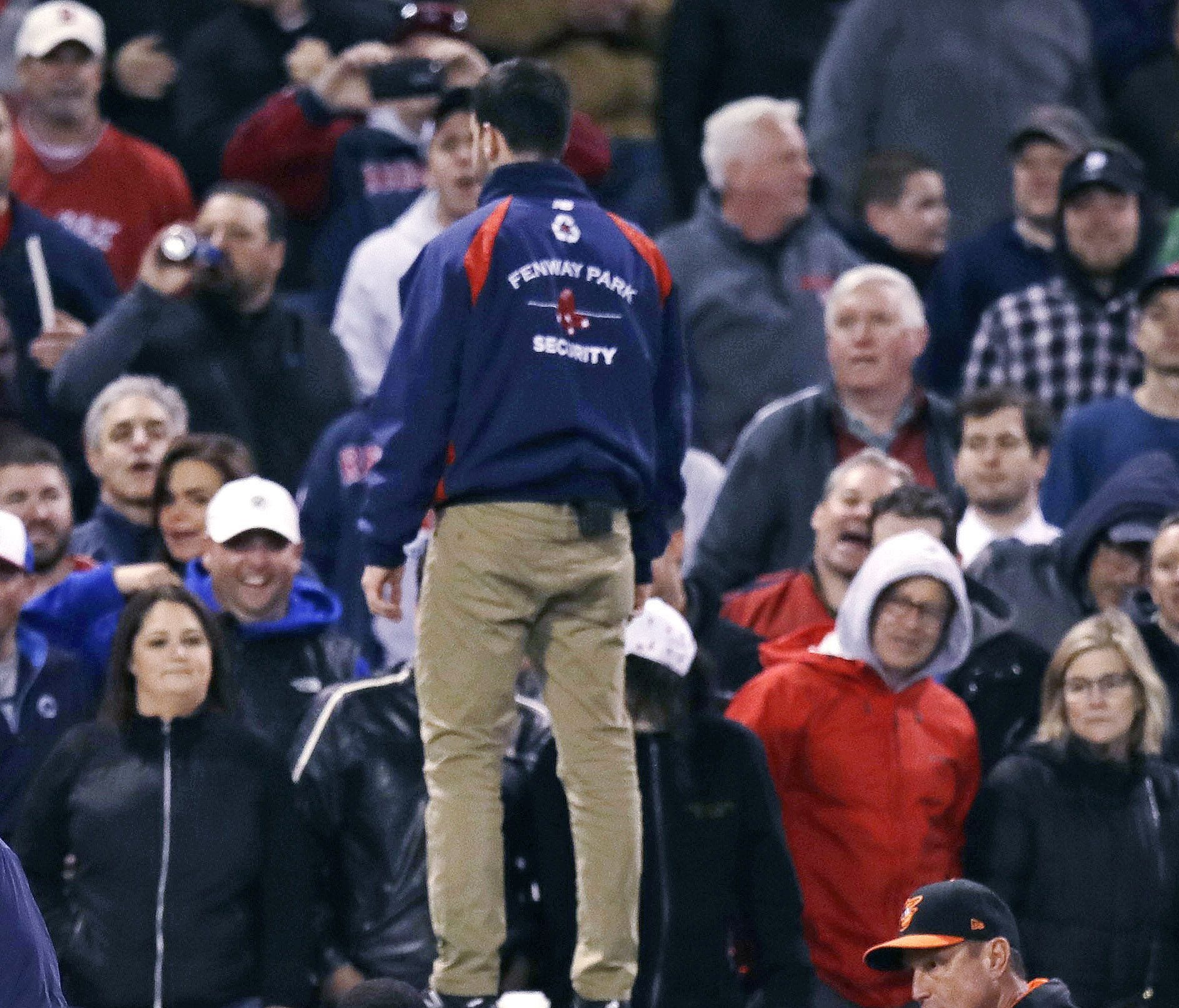 Security guard stands on the dugout roof as Red Sox fans watch.