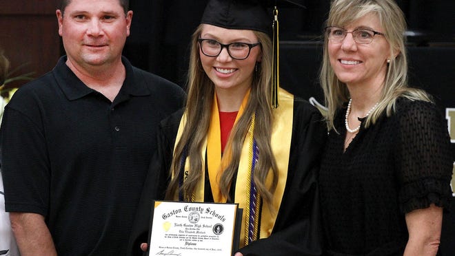 North Gaston senior Erin Medlock displays her diploma as she poses for a photo with family members during her graduation ceremony Monday.  Public school students across the county will have individual graduations with five to six scheduled an hour because of restrictions due to COVID-19.