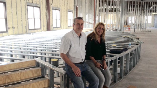 Tim and Julie Gilliland perch on the frame for the stage in the meeting area in the planned River Crossing Event Center where their Church out of Church intends to move.