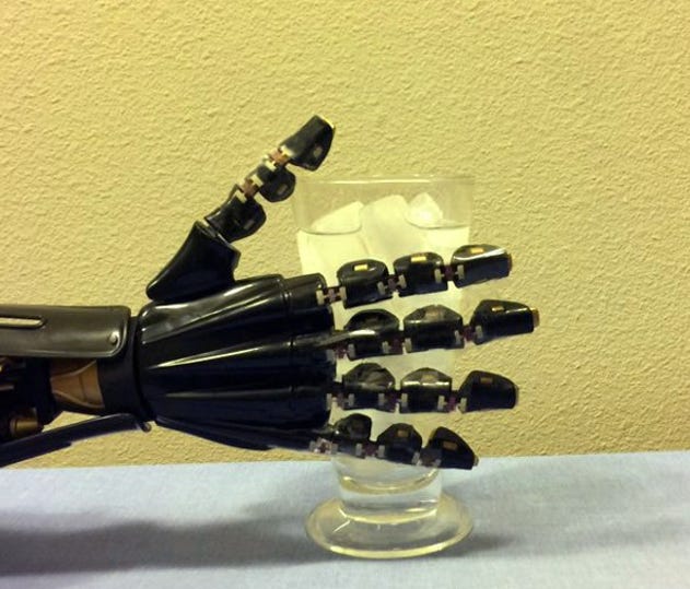 A robot hand with artificial skin reaches for a glass of ice water.