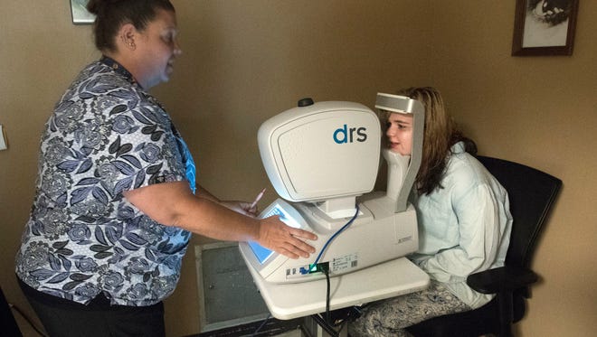 Medical assistant Wendi Adams, left, uses an IRIS retinal scanner to check Amber Coley's eyes June 22, 2017, at the Escambia County Community Clinic.