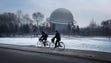 Two people cycle past a planetarium at the Three Revolutions