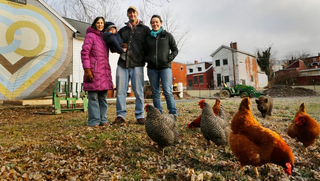 Grow the Cov urban farm members (from left) Janet Tobler, Gus Wolf, his son Gus, and Lydia Cook are photographed with chickens and the farm’s pot-bellied pig Rillette on Orchard Street in Covington.