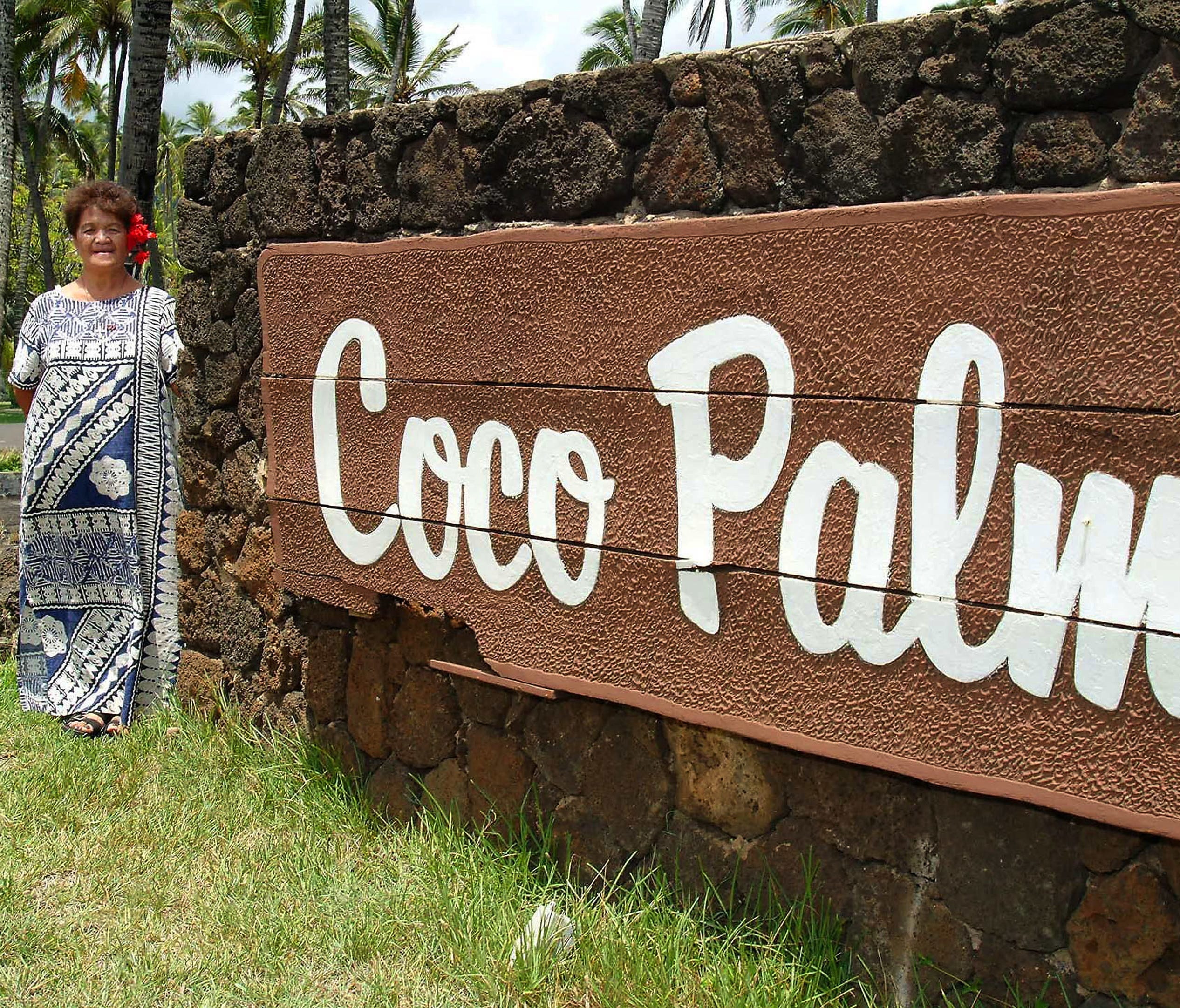 FILE - In this Sept. 4, 2002 file photo, Cecilia Dana poses for a photo beside a Coco Palms resort sign in Wailua on the island of Kauai in Hawaii. Native Hawaiian activists, who claim to be descendants of Kauai's last king, are occupying the propert