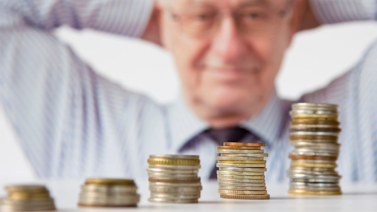 Older man with hands behind his head looking at five increasingly higher stacks of coins