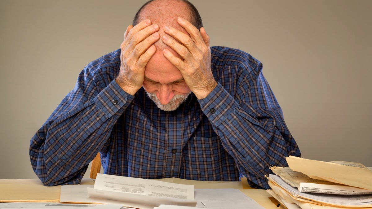 Older man holding his head while looking at papers.