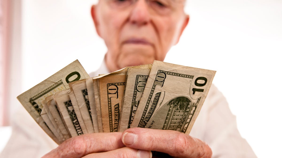 A senior man counting a fanned pile of cash in his hands.