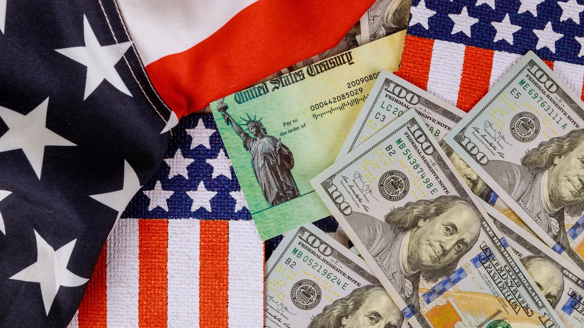 A stimulus check amid hundred-dollar bills and U.S. flags.