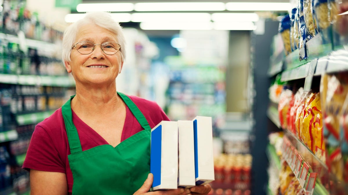 A smiling older woman at work stocking shelves
