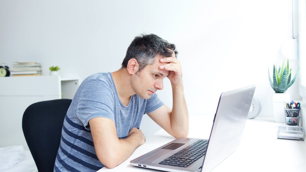 Man holding his head while staring at laptop screen
