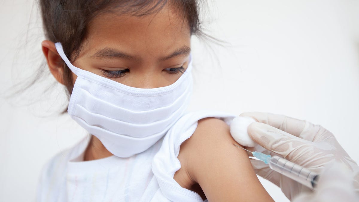 A girl wearing a mask receives an injection in her arm.