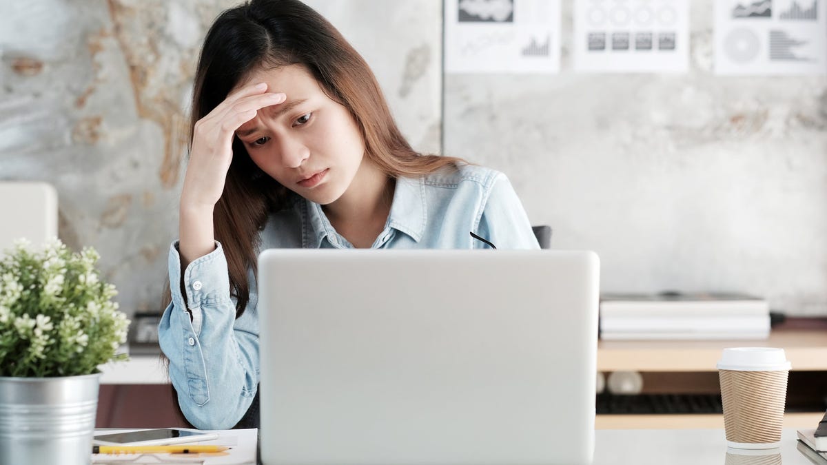 Woman at laptop resting hand on forehead and looking upset