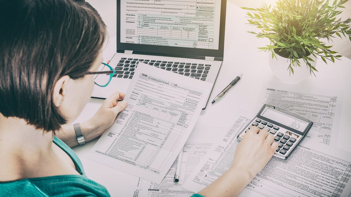 A woman looks at a tax return form and uses a calculator.