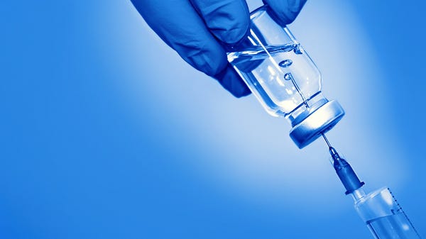 Gloved hand holding vaccine vial with a syringe an