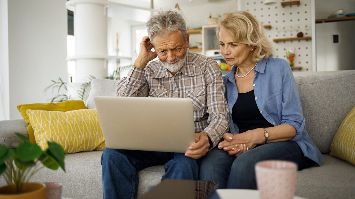 Older man and woman sitting on couch, looking at laptop