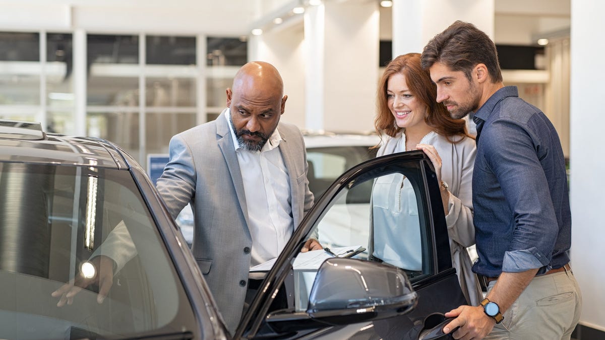 A couple shopping for a car as a salesperson shows them a car's interior.