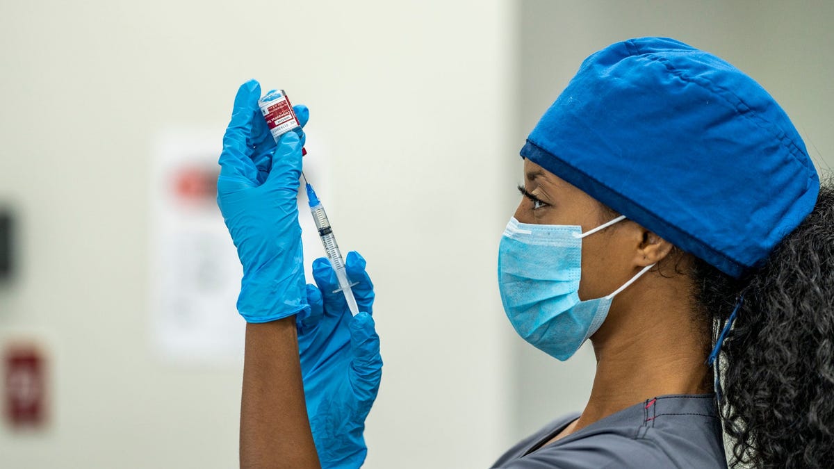 A healthcare professional holding a syringe and needle up to a vaccine vial.