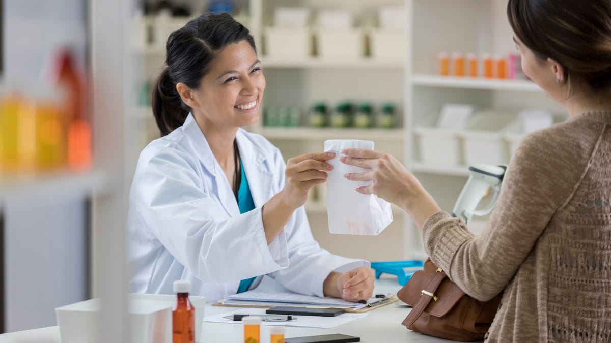 A person at a pharmacy counter hands a white bag to a customer.