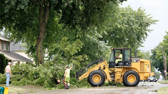 Employees of the Waupun Department of Public Works use a front-end loader to remove broken branches from the front yard of a home in Waupun. The wind storm that struck the city is called a "microburst."
