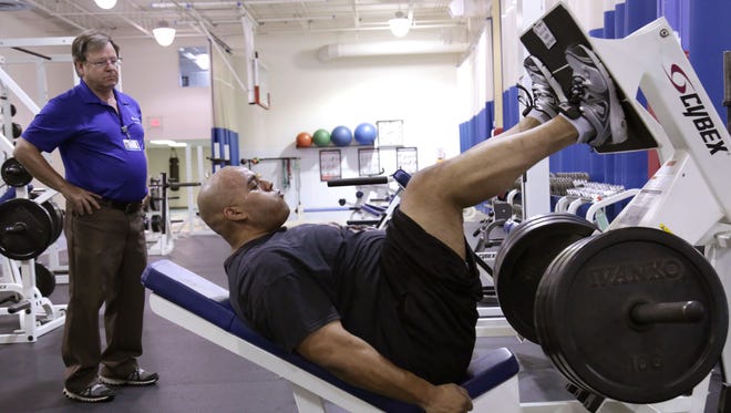 OhioHealth physical therapist Steve Rau watches Mansfield Police Sgt. Toneli Webb do leg presses Wednesday at the OhioHealth Health Ontario Health and Fitness Center. In November, Toneli sustained 19 injuries when he fell through the floor during a call.