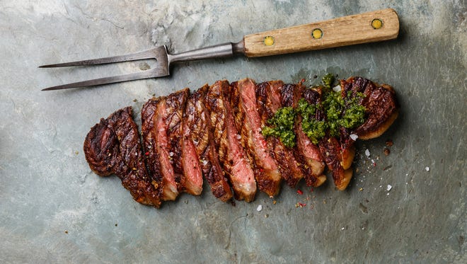 Sliced grilled beef barbecue Striploin steak with chimichurri sauce and meat fork on gray stone slate background