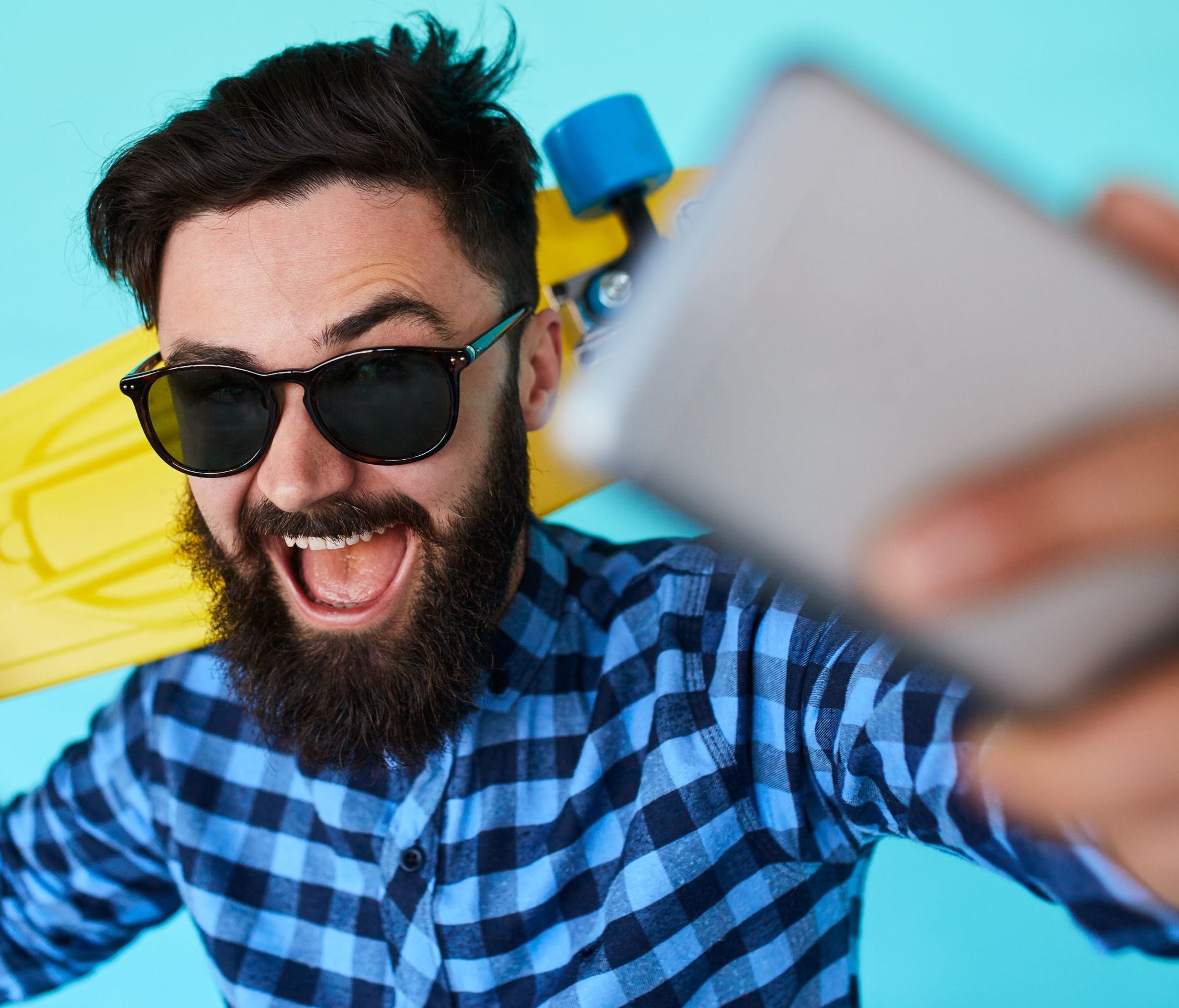 Young hipster with beard in glasses taking selfie and smiling.