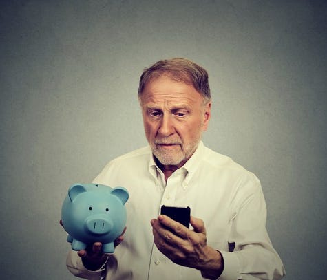 Older man holding a blue piggy bank and looking at a phone