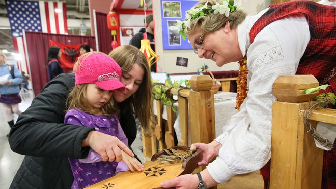 Sigrida Staks of Shorewood (right) shows Isla Noller of Elkhorn and her mother, Jessica, how to play the kokle, a Latvian instrument, at the Holiday Folk Fair International in 2015. The 2017 edition is this weekend at Wisconsin State Fair Park.
