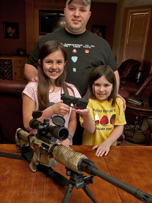 Nathan Gibson with his daughters Meredith, 10, left, and Natalie, 8, right, at their Johnston home on Tuesday afternoon April 15, 2014.  The girls are holding a Walther 22, a handgun they are no longer allowed to shoot, but on the table is a .308 deer rifle that under the law they could fire. Gibson has been taking his two daughters to a shooting range in Polk City since they were 5, and this past weekend he and Natalie were told to leave because she’s not old enough to practice with her handgun.