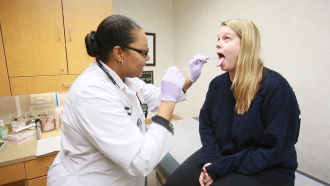 Nurse practitioner Kimberly Page, 41, Oak Park, left, swabs the tonsils of Meghan Faught, 21, of Royal Oak for a strep test at the CVS Minute Clinic in Southfield on Wednesday, Feb. 4, 2015. Faught says she came to Minute Clinic because it is convenient.