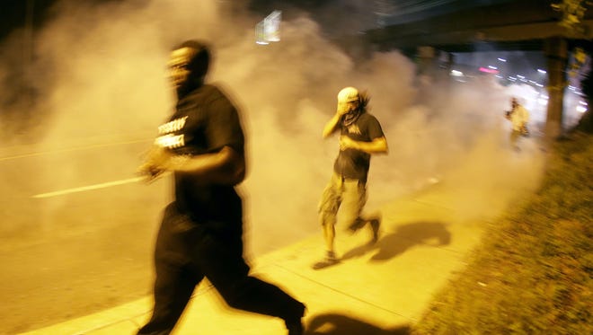 People run from tear gas after police dispersed a crowd on Aug. 17, 2014, during a protest in Ferguson, Mo.