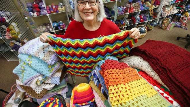Karen Taylor, owner of Yak 'n Yarn, stands next to a pile of knitted and crocheted items made by volunteers. Taylor has organized a sock drive for the second year, and collected items will be distributed to local nonprofits, the Colmery O'Neil VA Medical Center and Topeka Unified School District 501.