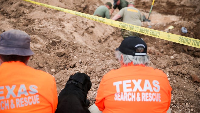 Orion, a human remains detection dog, sits between Texas Search and Rescue workers as a Tom Green County Sheriff's crew uncovers a body Wednesday, March 8, at the former San Angelo Speedway on Farm-to-Market Road 2105.