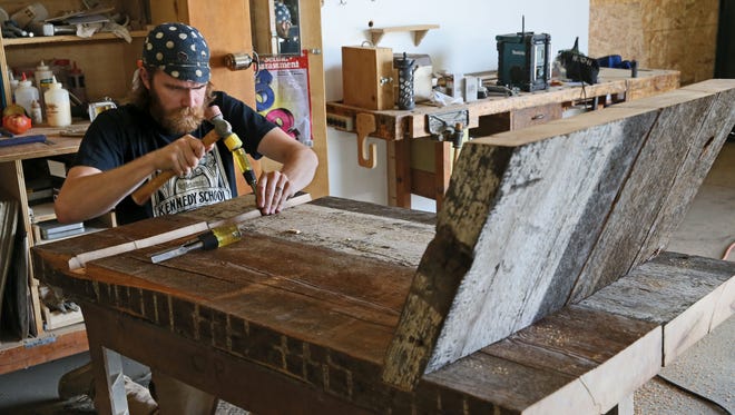 Corey Prendergast, an employee at Scathain, a furnishings manufacturer that has gone through the growth program of Scale Up Milwaukee, works on what will become a mirrored cocktail table made of barn wood.
