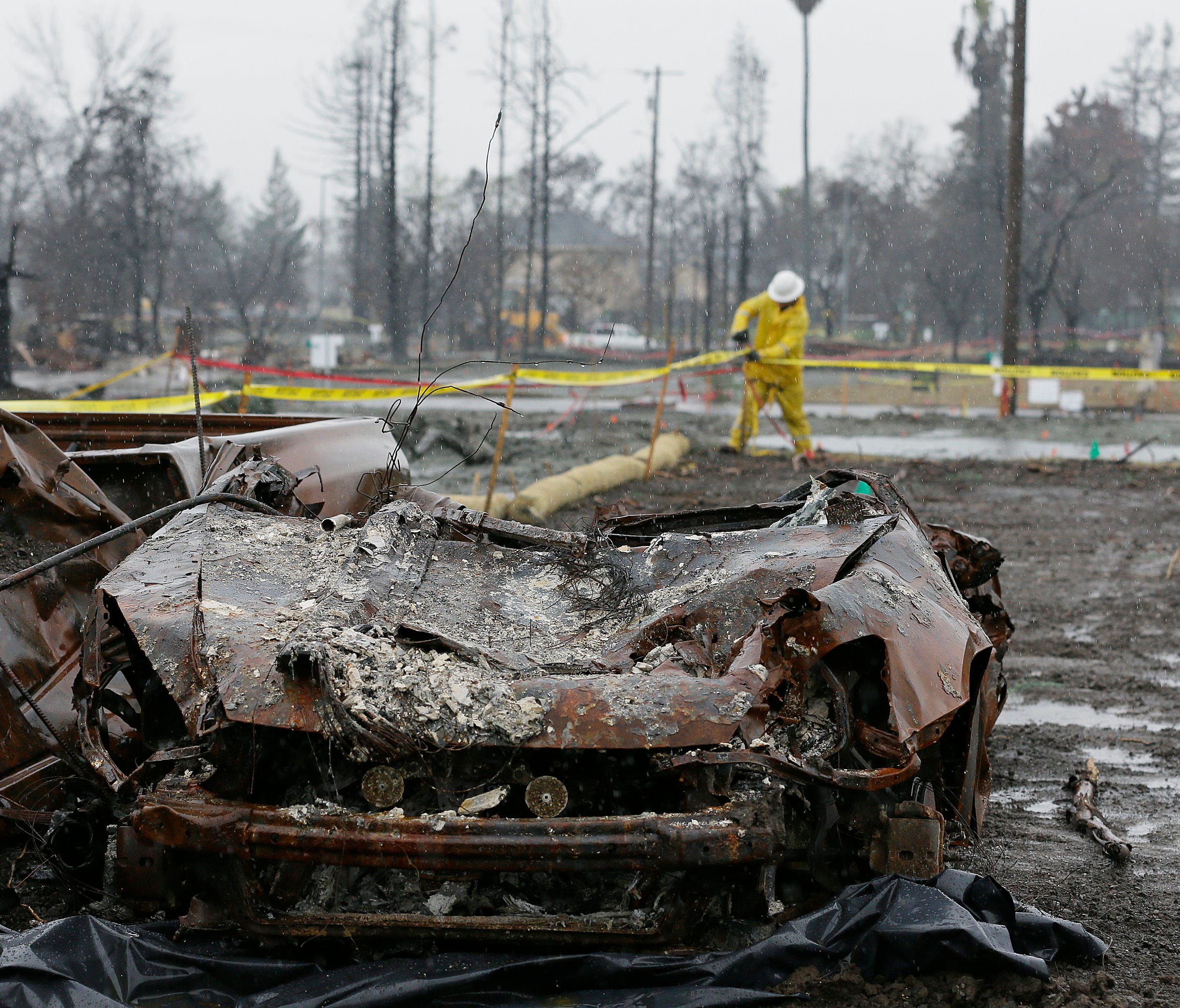 With a burned car in the foreground a worker finishes up erosion control efforts in the wildfire damaged Coffey Park neighborhood, Monday, Jan. 8, 2018, in Santa Rosa, Calif.