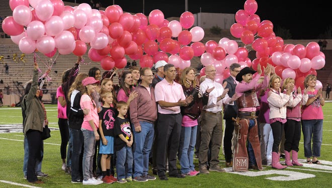 NMSU administrators, community leaders, cancer survivors and their loved ones including representatives of the Tough Enough to Wear Pink fundraising organization, gather on the football field at Aggie Memorial Stadium during a special halftime presentation at the Tough Enough to Wear Pink homecoming football game. The group assembled to honor funds raised for cancer research and to remember those who lost their battle to cancer. The group released pink balloons into the air as part of the presentation.
