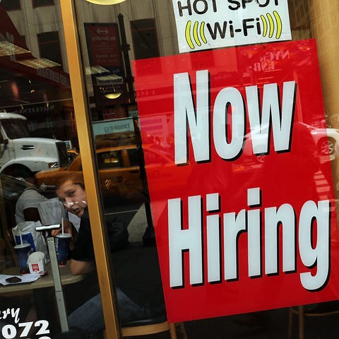 A "now hiring" sign is viewed in the window of a b
