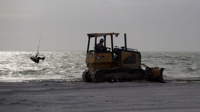 Work progresses on the Lovers Key beach renourishment project Tuesday while a kite boarder enjoys the high winds.