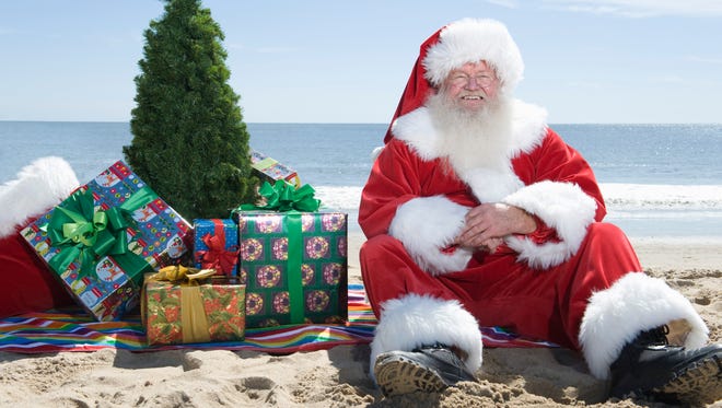 Father Christmas sits on the beach with a tree and presents