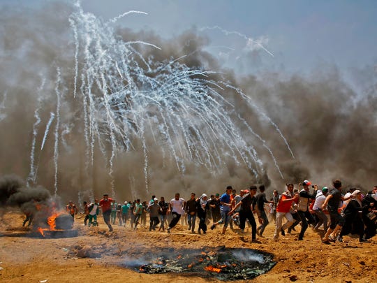 Palestinians run for cover from tear gas during clashes with Israeli security forces near the border between Israel and the Gaza Strip, east of Jabalia on May 14, 2018, as Palestinians protest over the inauguration of the US embassy following its controversial move to Jerusalem.