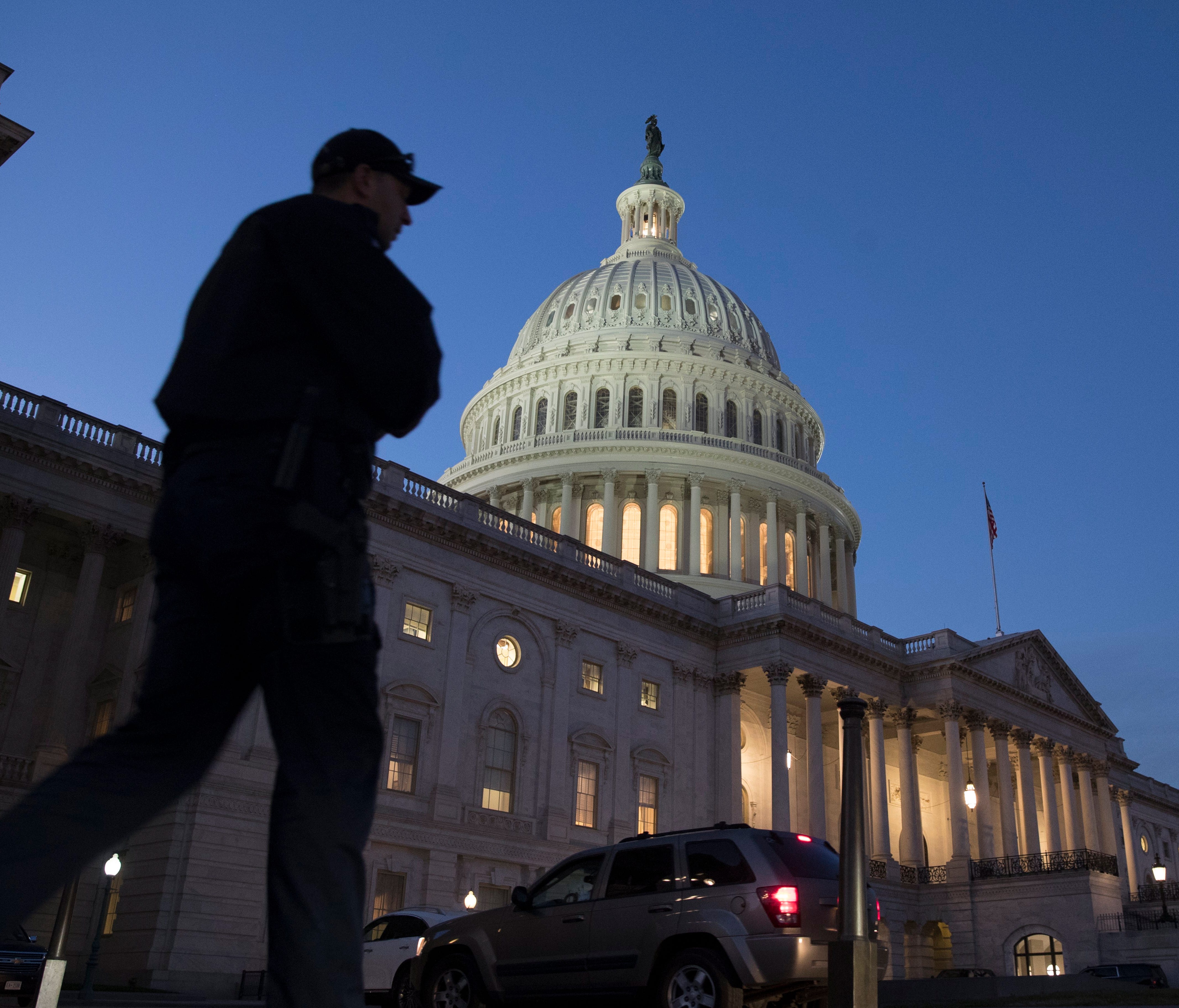 A Capitol police officer walks in front of the Capitol building at dusk after the House passed a short-term measure to fund the federal government.
