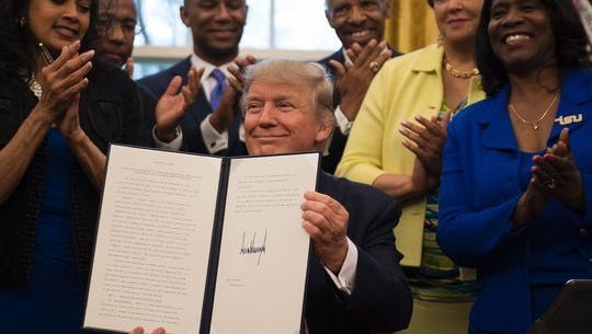 President Donald Trump (center) holds up an executive order to bolster historically black colleges and universities after signing it in the Oval Office of the White House in Washington, on Feb. 28, 2017.