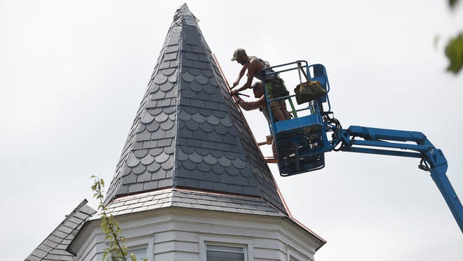 Working high above Annville Steve Seyfert (closest to camera) replaces roofs that have lasted hundreds of years. He hopes the replacement roofs he builds will last equally long. Seyfert uses a bucket to work on the Fortna building in Annville.
