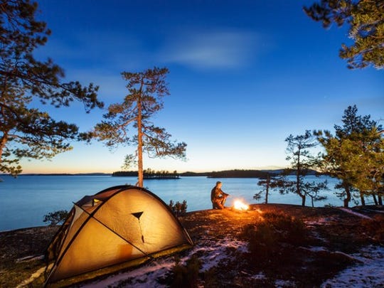 A camping tent and a man by a campfire by a lake