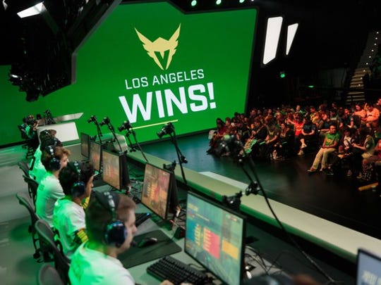 Overwatch League team members, Los Angeles Valiant, sitting in front of a computer with a sign saying "Los Angeles wins!"
