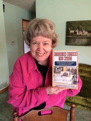 Suzanne Kelly poses with a copy of her new book, “Reaching Beyond the Waves,” a chronicle of her sixth-grade class’s remarkable project.