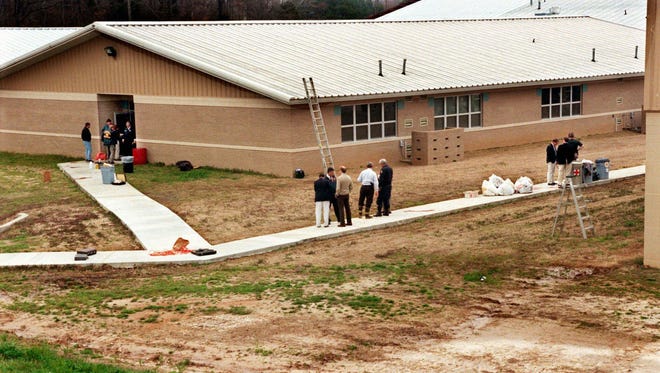 In this March 24, 1998 file photo, officials examine the scene at Westside Middle School in Jonesboro, Ark. after two boys fired on teachers and students. The two boys with stolen guns took aim from a wooded hill, waiting for people to evacuate after one of the boys had triggered a false fire alarm. They killed four children and a teacher.
