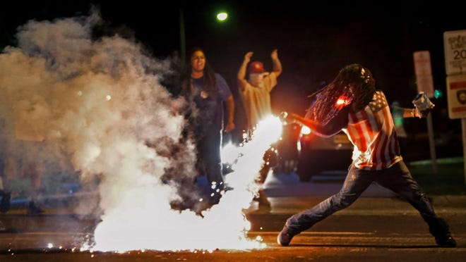 In this Aug. 13, 2014, file photo Edward Crawford Jr., returns a tear gas canister fired by police who were trying to disperse protesters in Ferguson, Mo.