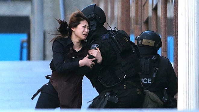 A hostage runs to armed tactical response police officers for safety after she escaped from a cafe under siege at Martin Place in the central business district of Sydney on Monday.