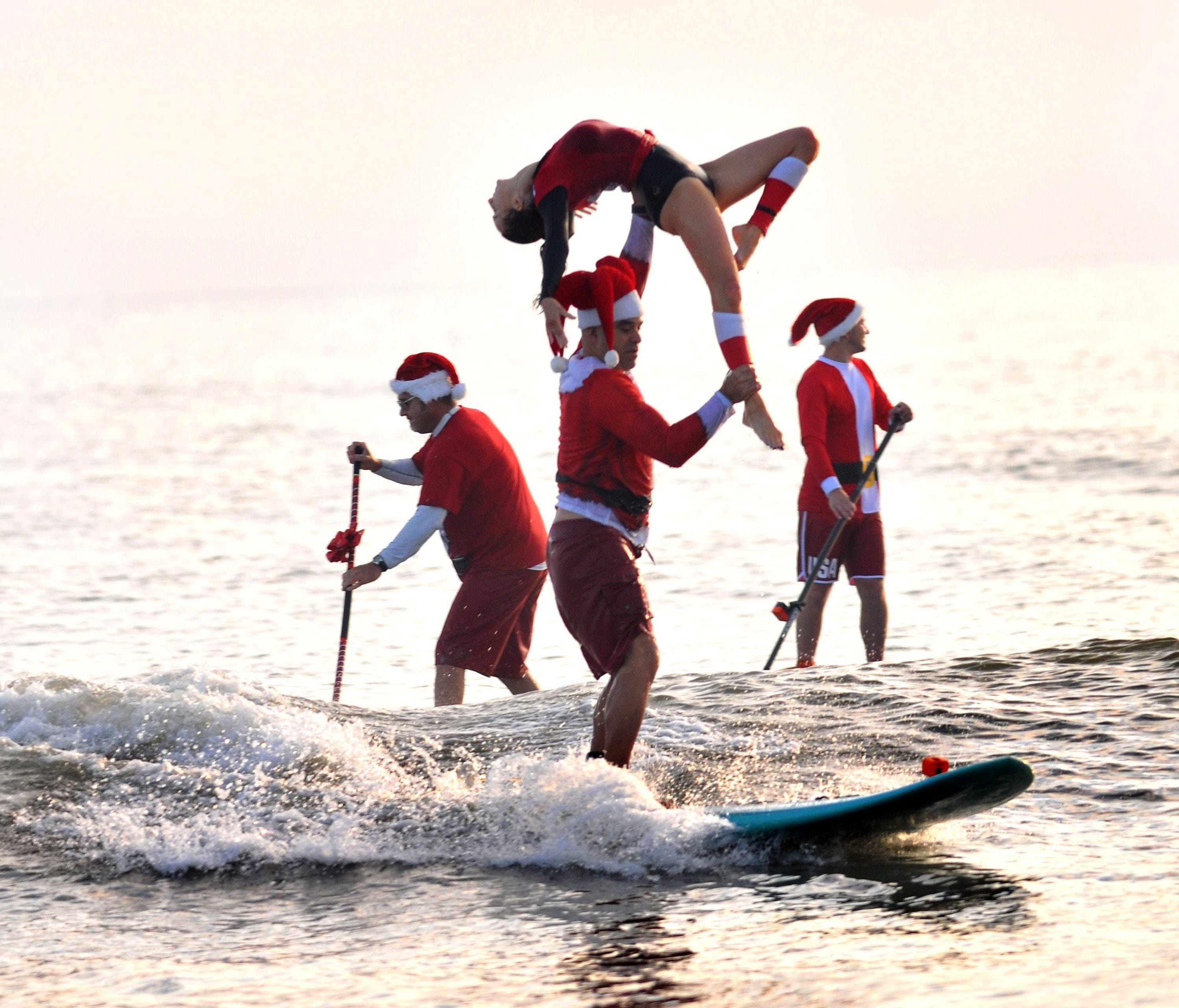 Ed and Kymmie Martinez of Cocoa Beach, Fla., do some tandem sufing Dec. 24, 2017, surfing past two of the hundreds of Surfing Santas that had gathered at Cocoa Beach for the ninth year..